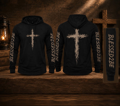 Two black hoodies displayed on a rustic wooden surface, showing the front and back views. The hoodies feature a distressed white cross graphic on the chest and the text 'BLESSED 2BEE' printed vertically down the sleeves.