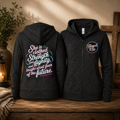 Two dark heather zip-up hoodies displayed side by side on a rustic wooden surface. The left hoodie shows the back with a large colorful inspirational Bible verse in white, pink, and blue text.