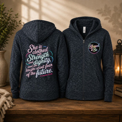 Two navy heather zip-up hoodies displayed on a wooden table, showing the front and back. The front hoodie has a circular 'Blessed 2 Be' graphic on the left chest, and the back hoodie features a large inspirational quote in pink, teal, and white script.
